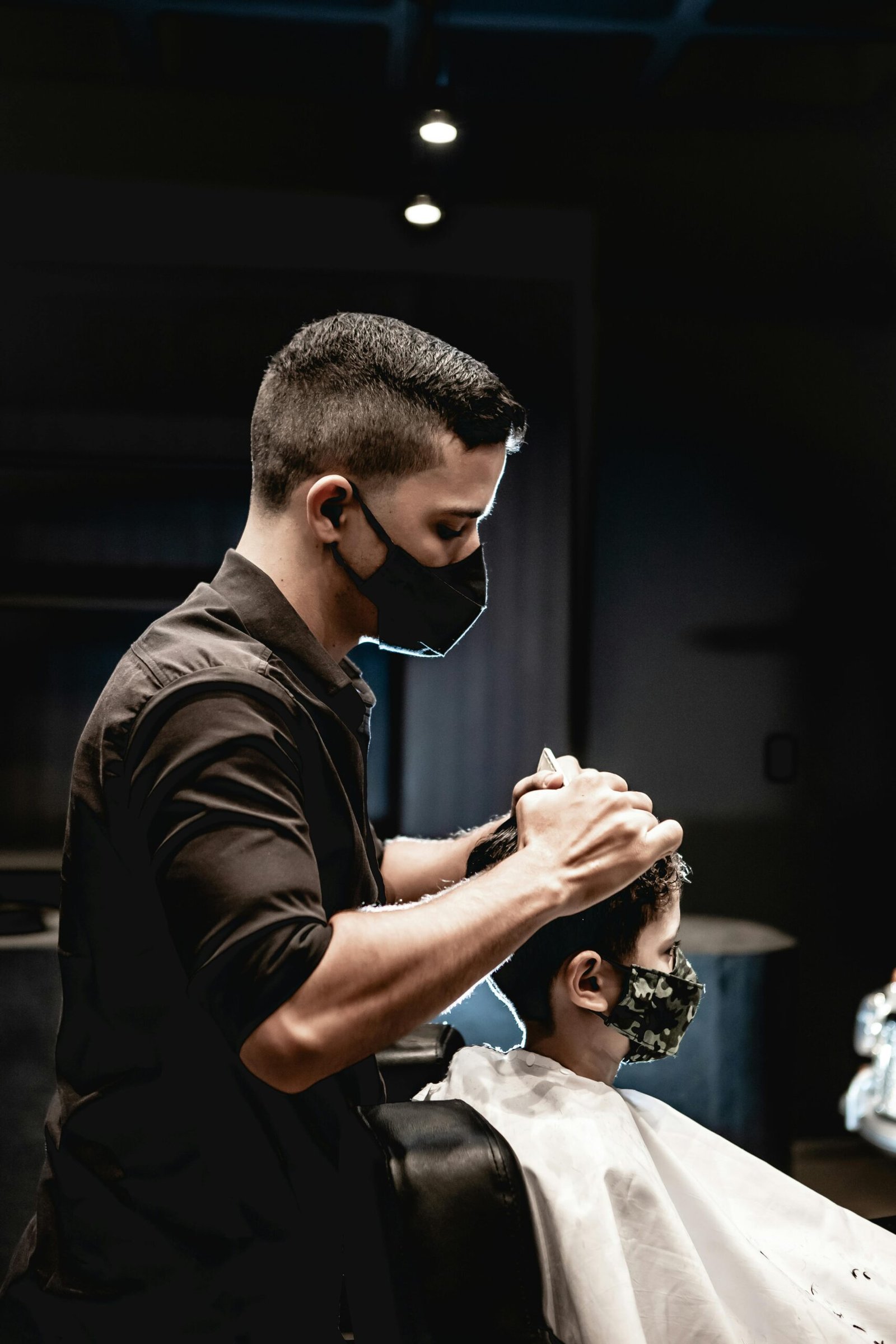 A barber in João Pessoa, Brazil, cuts a young boy's hair as both wear face masks, emphasizing safety.